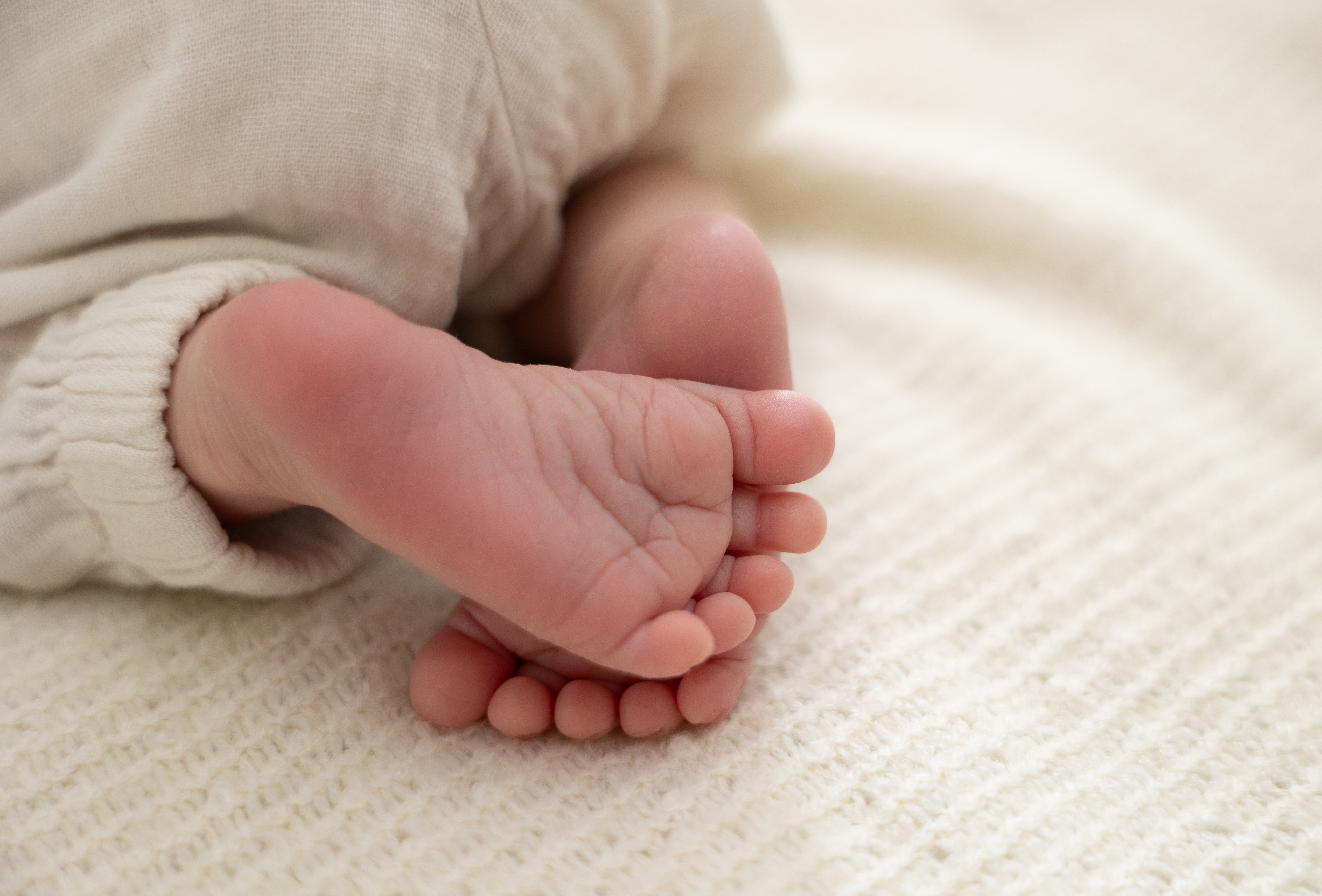 Nahaufnahme von Babyfüßen auf einer hellen, weichen Decke.